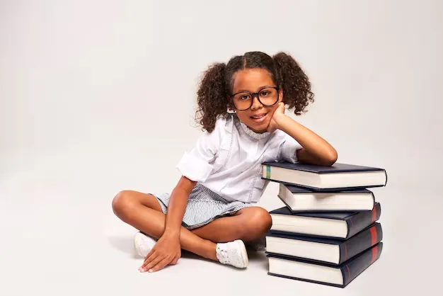 Petite fille assise à côté d'une pile de livres