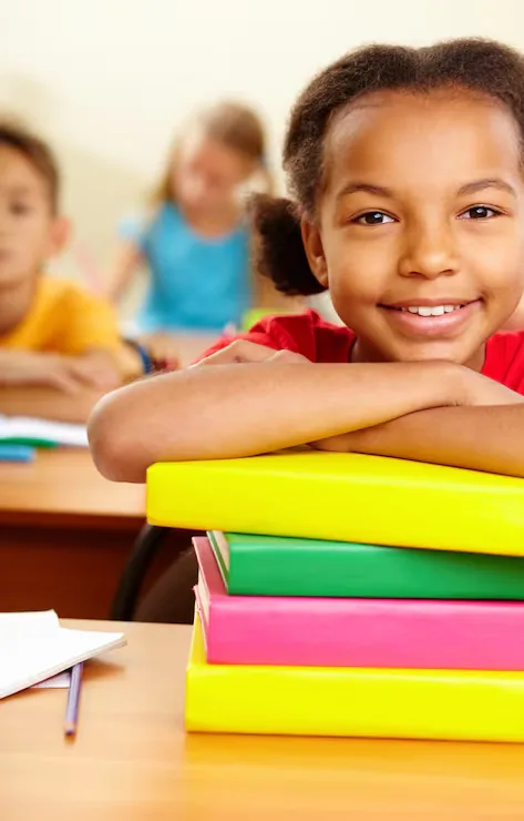 Élève souriante appuyée sur une pile de livres