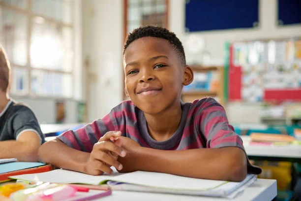 Élève souriant qui écrit dans son cahier en classe